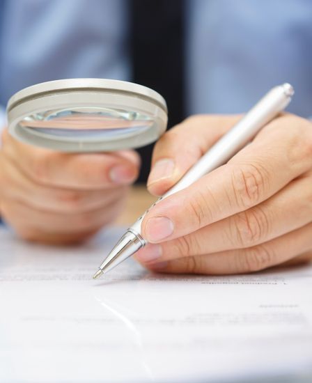 Two hands holding a magnifying glass and a pen