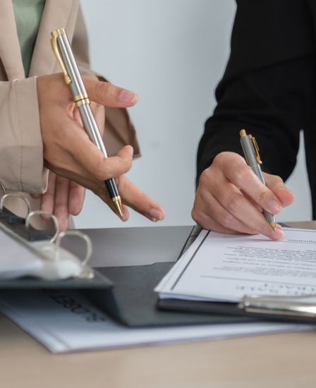 Two hands holding pens going over a document