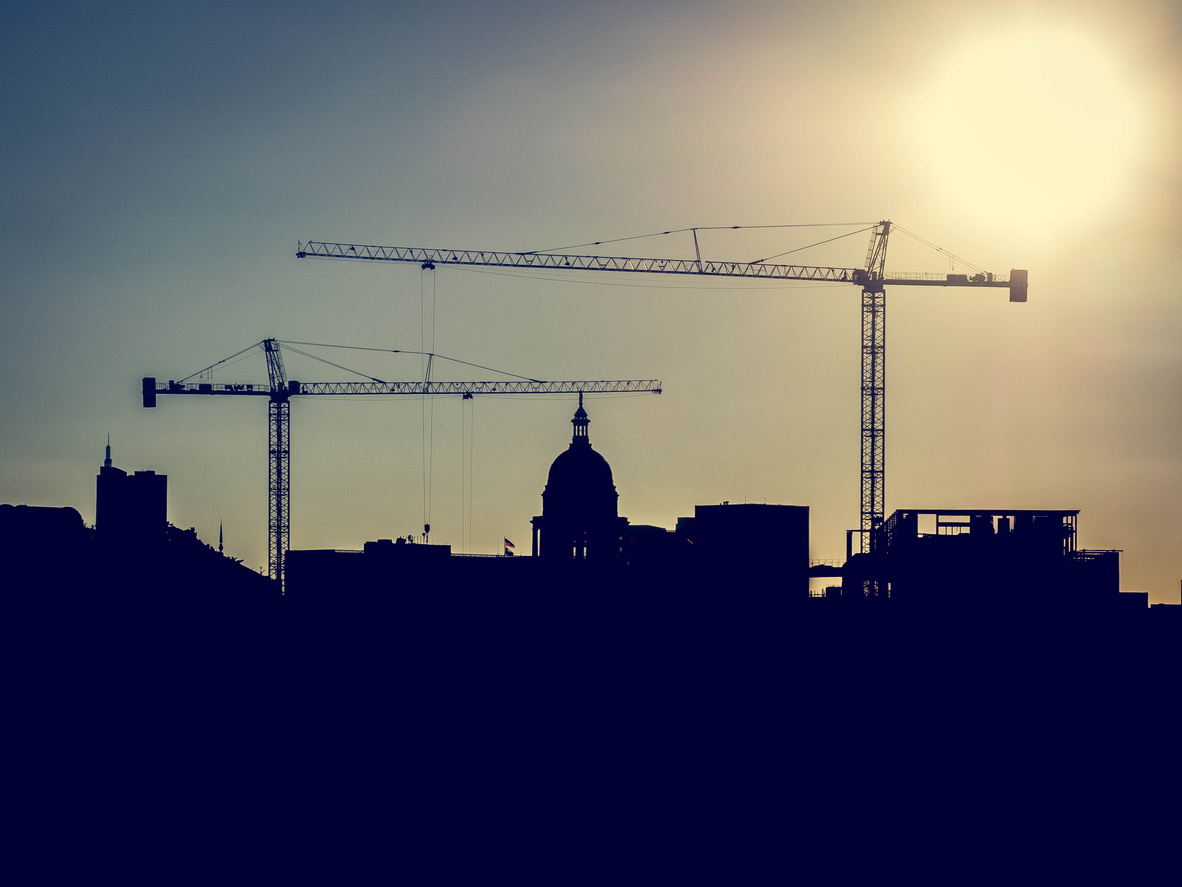 A Silhouette of the Austin, Texas Capital Building framed by construction cranes at sunset.